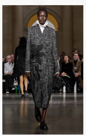 Model walking at London Fashion Week Fall/Winter 2026 wearing oversized sculptural coat with exaggerated shoulders.