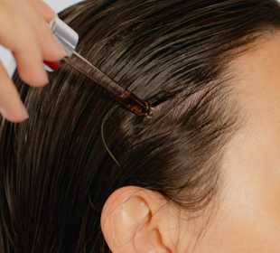 a woman applying hair oil on her hair