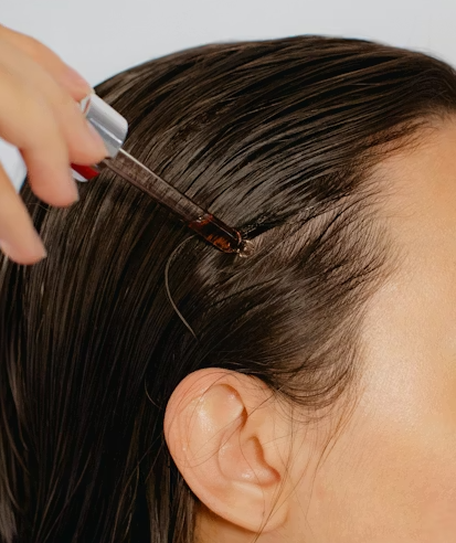 a woman applying hair oil on her hair