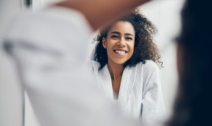 Woman practicing free self-care at home by looking her reflection on the mirror
