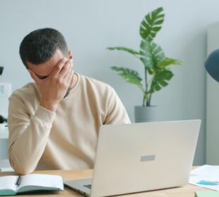 Person at desk showing emotional burnout symptoms with head in hands