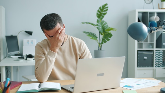 Person at desk showing emotional burnout symptoms with head in hands