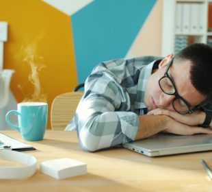 a man sleeping on a desk with coffee and laptop