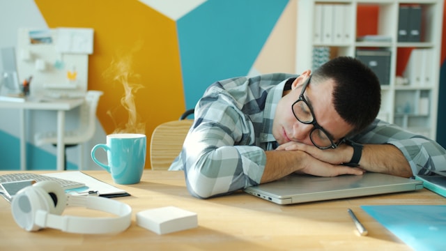 a man sleeping on a desk with coffee and laptop